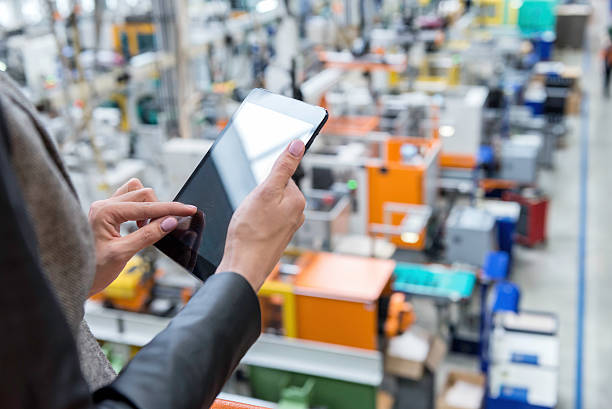 Woman standing on top of a balcony, holding touchpad and checking inventory of a manufacturing company on touchscreen tablet.