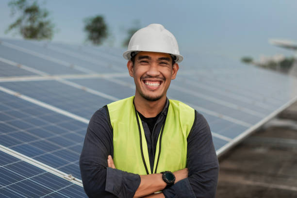 Engineer man standing and smiling with arms crossed with solar panels energy. Technician checking and services of photovoltaic solar panels. Sustainable Energy concept.