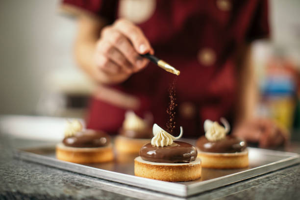 woman decorating chocolate cookies with sweet powder on top. She works in sweet food manufacture, small business company