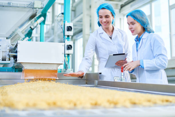 Waist up portrait of female workers wearing lab coats standing by conveyor line