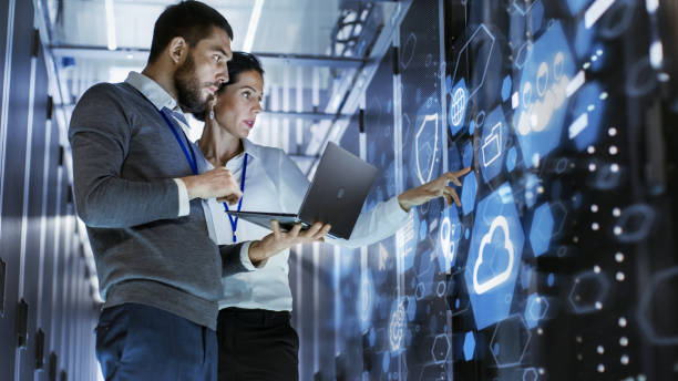 Cloud Computing. IT Specialist Holds Laptop and Discusses Work with Server Technician. Standing in Data Center, Rack Server Cabinet with Cloud Server