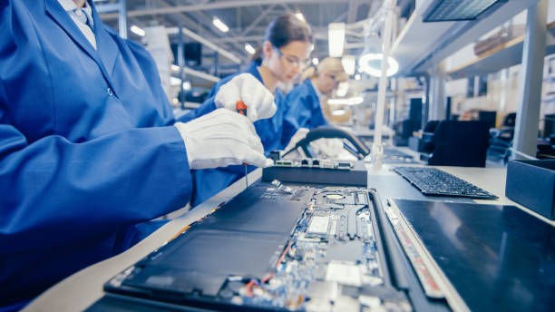 Electronic Manufacturing Process. Electronics Factory Worker in Work Coat Assembling Laptop's Motherboard with Screwdriver