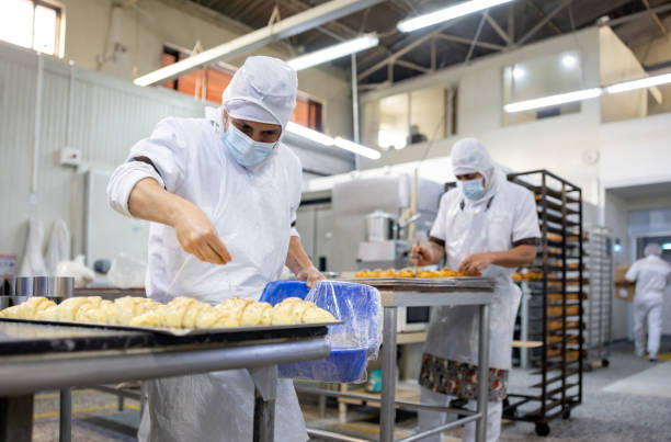 baker working at an industrial bakery and sprinkling sesame seeds on a croissant