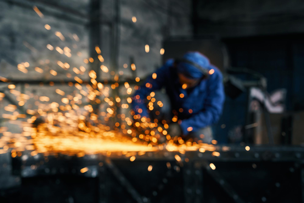 A blurred image of a welder sparking while working, with bright orange sparks flying against a dark industrial background