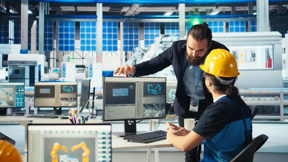 Industrial engineer and CNC technician discussing real-time production data on computer screens in a smart manufacturing facility using IoT technology