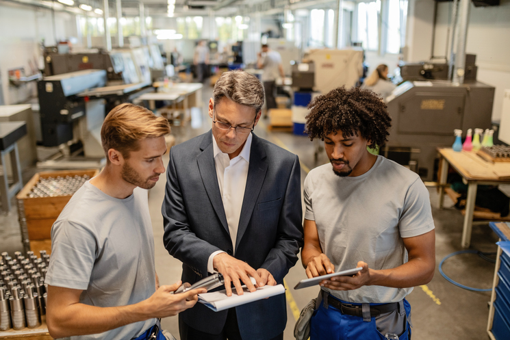 Mid adult engineer and steel workers reviewing quality reports in industrial building for quality management in manufacturing